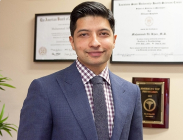 Dr. Khan smiling in front of his medical degrees and awards
